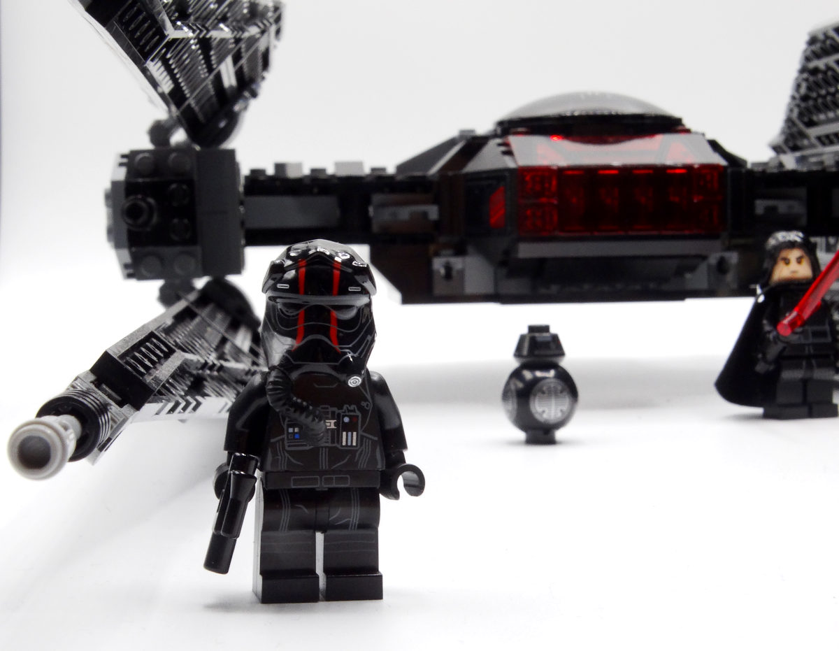 Tie-Pilot-Minifigur mit Blasterpistole vor dem Tie silencer, im Hintergrund stehen BB-9E und Kylo Ren mit rotem Lichtschwert.